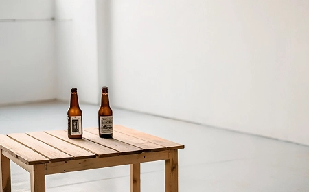 Две бутылки пива на деревянном столе в пустой белой комнате